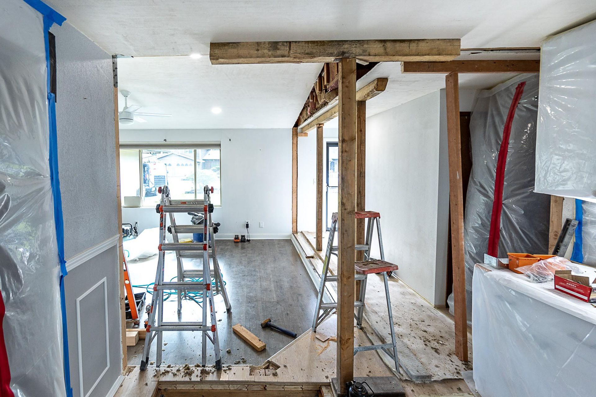 Interior renovation, room walls partially demolished. Wood framing and ladder visible. Covered kitchen area.