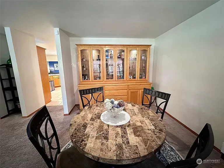Dining room with a round table, chairs, and a wooden cabinet. A hallway leads to the kitchen.