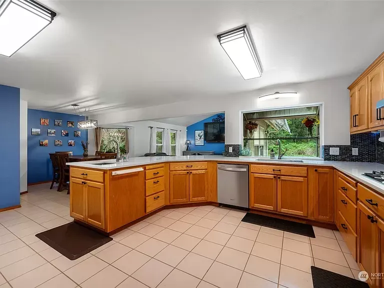Spacious kitchen with wood cabinets, white countertops, and stainless steel appliances. Blue walls and tile floor.
