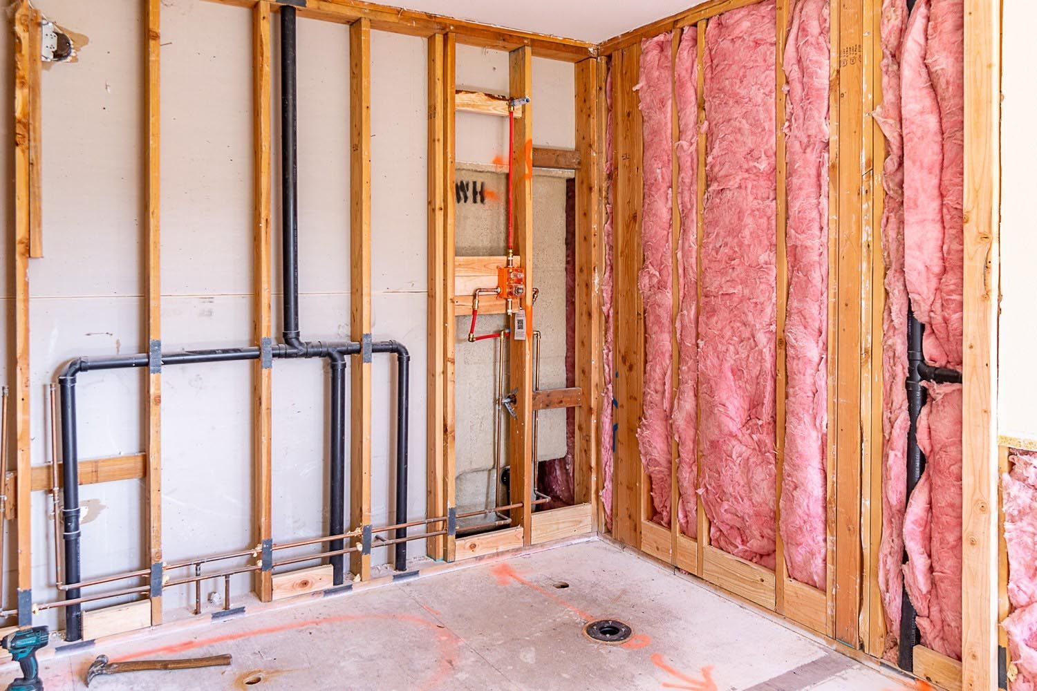 Bathroom renovation: exposed wall studs, plumbing, insulation, concrete floor.