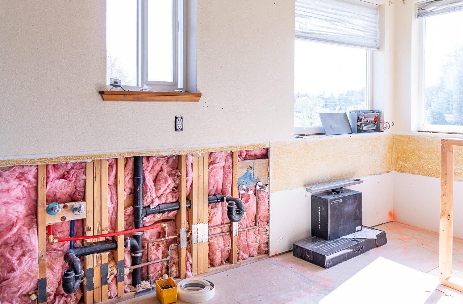 Interior of a room under renovation, with exposed pipes and pink insulation in the walls.