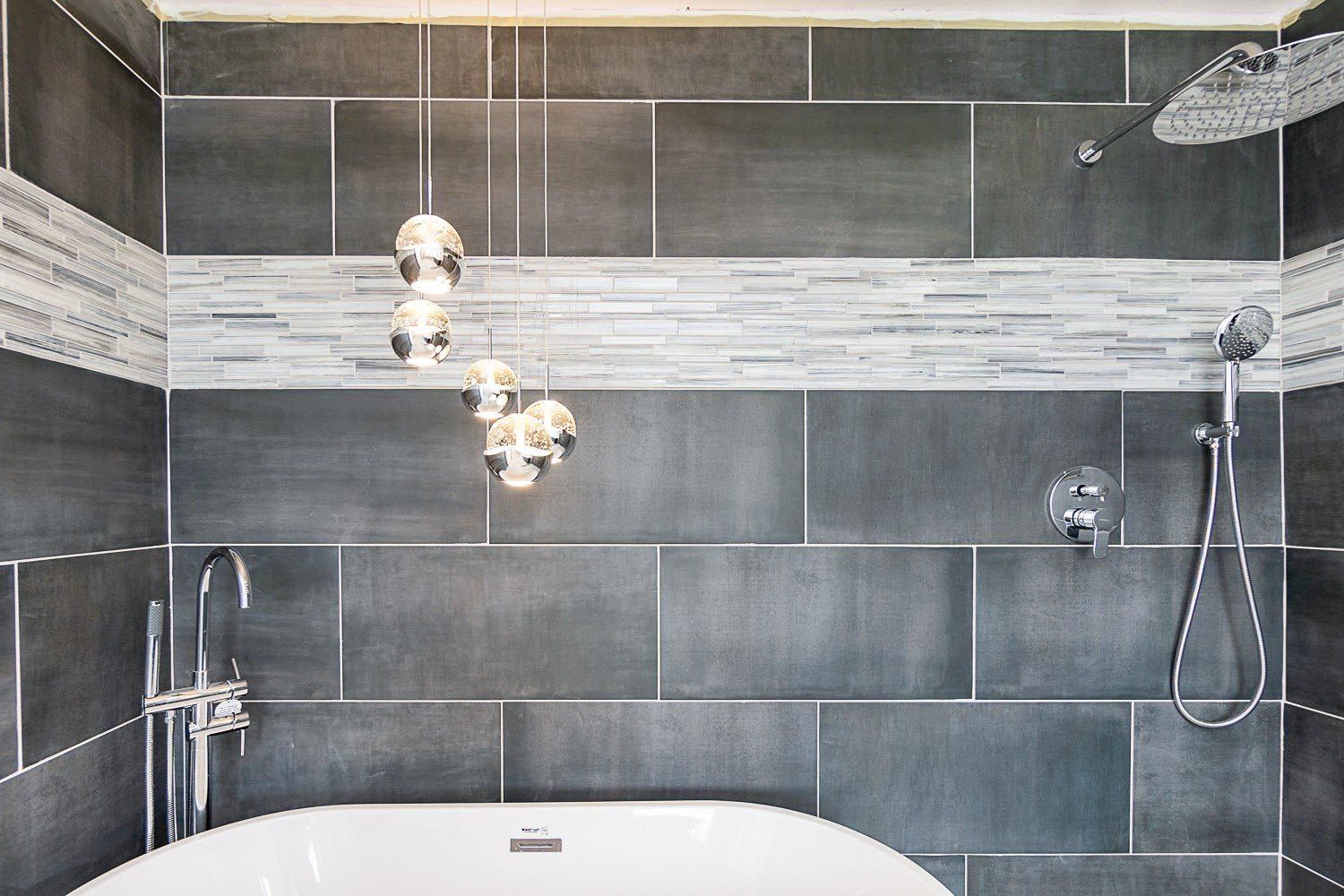 Gray-tiled bathroom with white bathtub, overhead shower, and skull-shaped hanging lights.