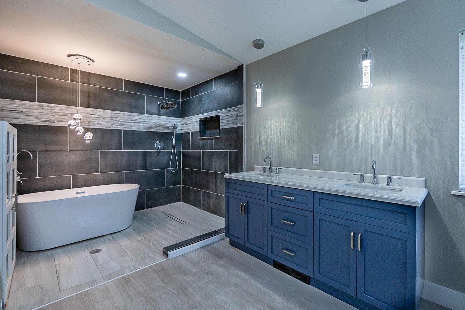Modern bathroom with blue vanity, gray walls, tile shower, and freestanding tub.