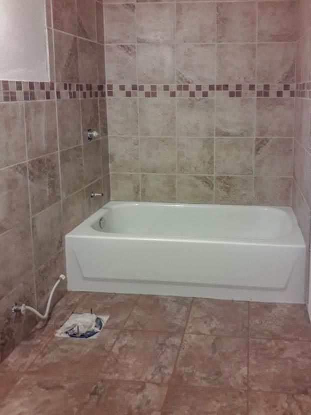 Bathroom with tiled walls and floor, white bathtub.