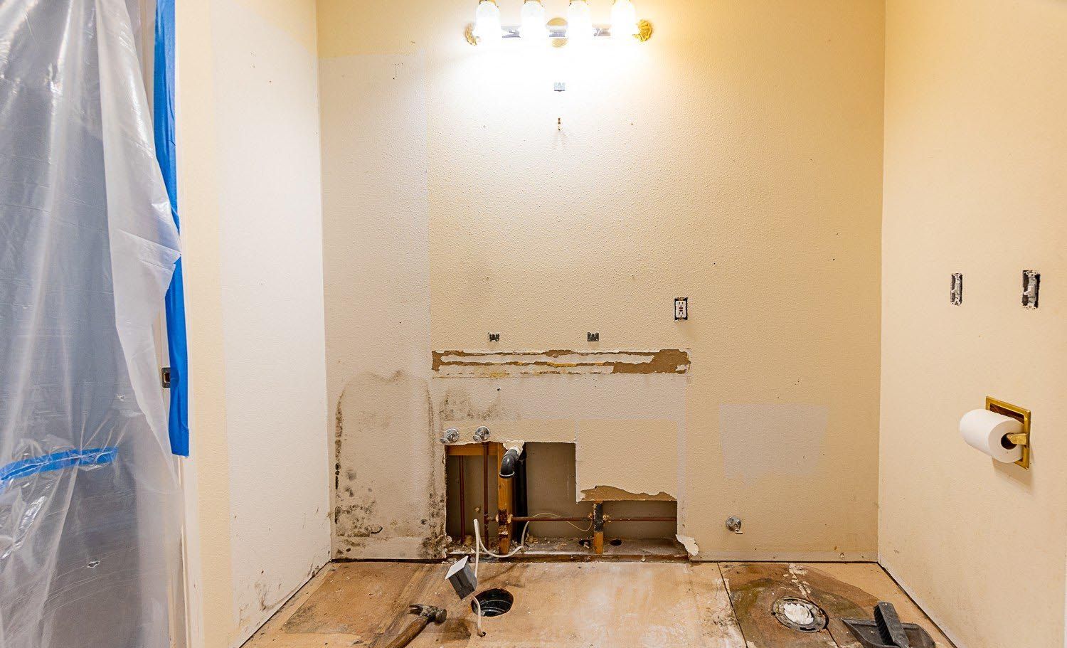 Bathroom under renovation with exposed plumbing, unfinished walls, and a toilet paper holder on the right.