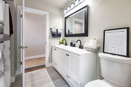 White bathroom with vanity, mirror, toilet, and open doorway to another room.