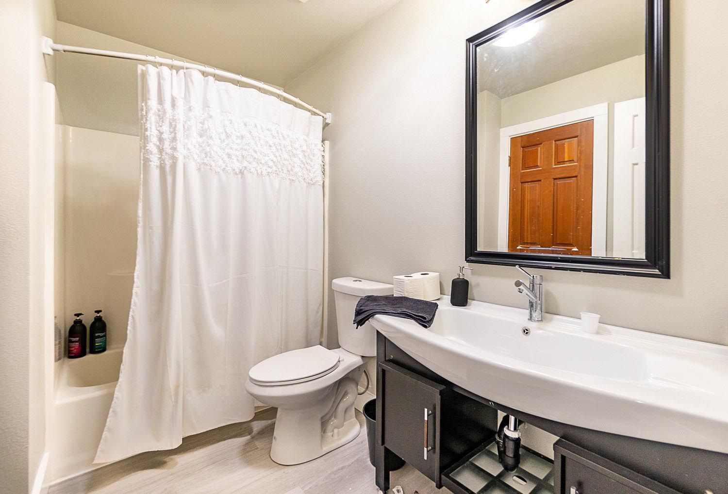 Bathroom with shower, toilet, sink, and mirror; white and gray color scheme.