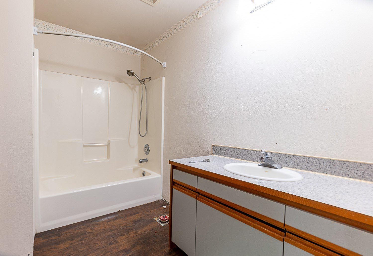 Bathroom with white shower and vanity, brown countertop, and dark wood-look floor.