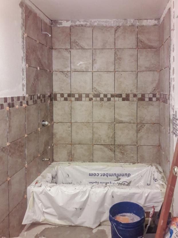 Bathroom shower tiled in progress; tan square tiles, mosaic border, bathtub covered.