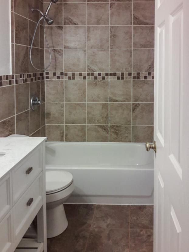 Bathroom with a white tub, toilet, and vanity, and brown tiled walls and floor.