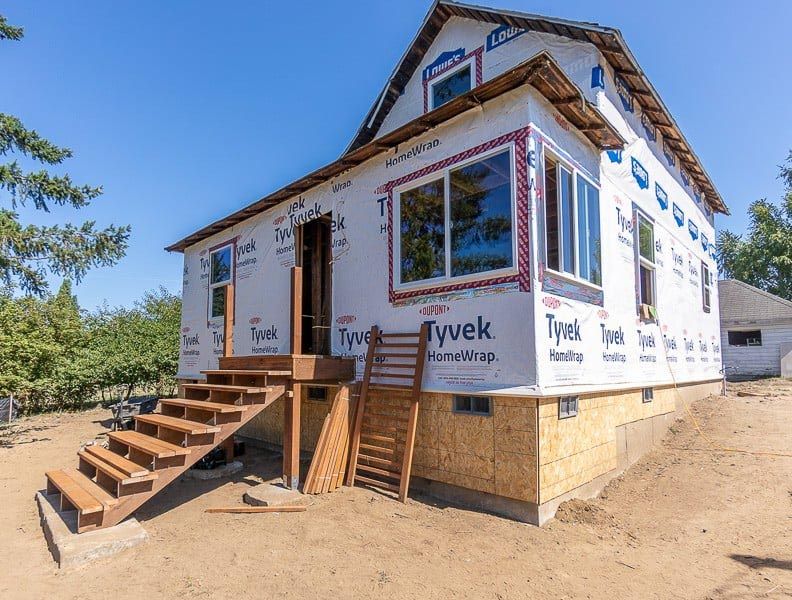 House under construction with wood stairs and windows, covered in Tyvek.