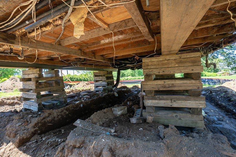 Underside view of a house raised on wooden blocks during foundation repair.