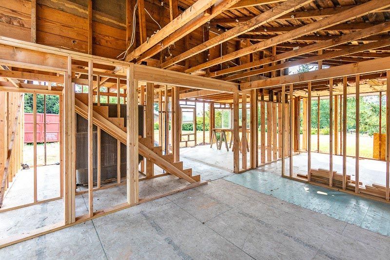 Interior view of a house under construction with exposed wooden framing and a concrete floor.