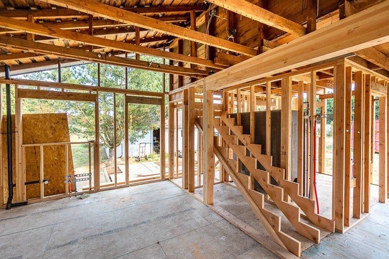 Interior of a building under construction, wooden framing visible with staircase and large windows.