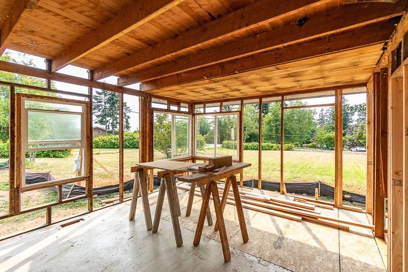 Wooden framework of a room under construction with a lawn in the background. A work table sits in the center.