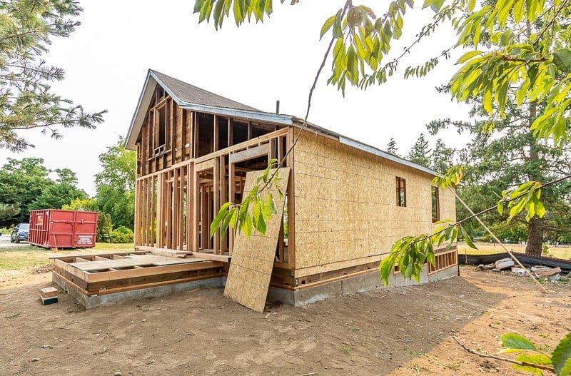 Building under construction; wooden frame, partially sheathed with OSB, a small porch, outdoors.