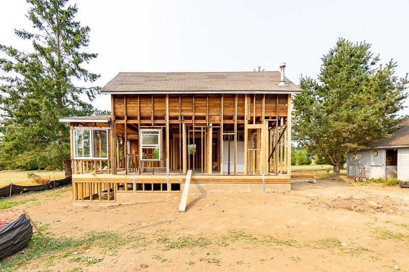 House under construction; exposed wooden frame; front porch; backyard setting.