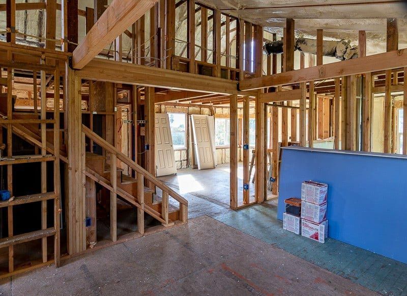 Interior of a house under construction; exposed wooden framing, stairs, doorways, and blue drywall.