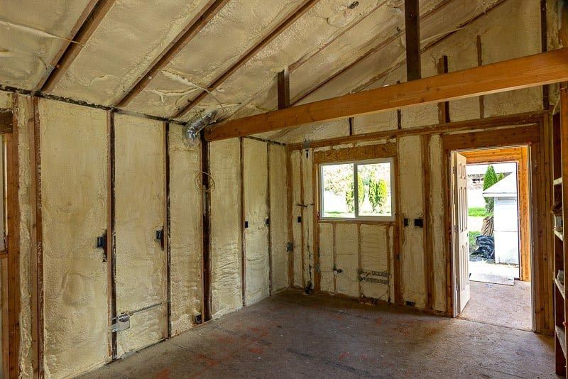 Interior of a room with exposed wooden beams and spray foam insulation on the walls.