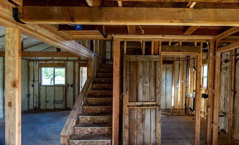 Interior of a building under construction, showing wooden framing, stairs, and exposed insulation.