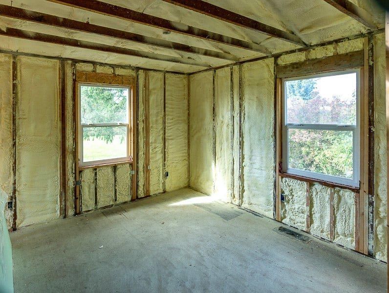 Interior room with spray foam insulation on walls and ceiling, two windows, and exposed studs.