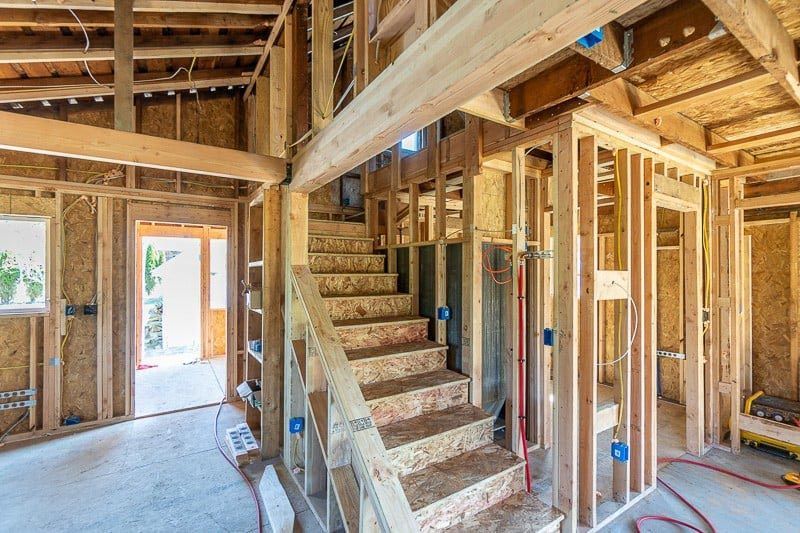 Interior view of a building under construction, showing wooden framing, staircase, and open doorways.