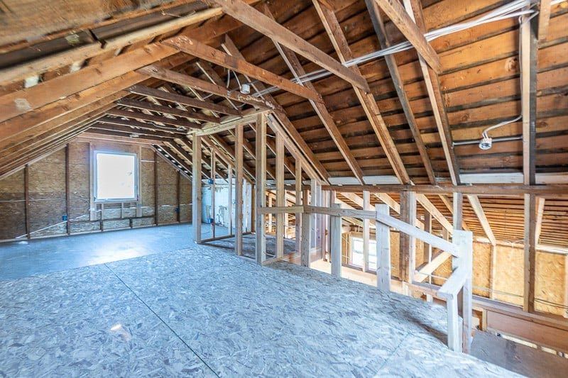 Unfinished attic interior with wooden beams, framing, and plywood floor.