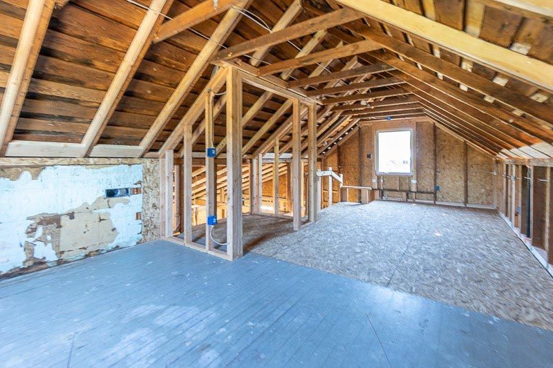 Unfinished attic with wooden framing, exposed beams, and a window.
