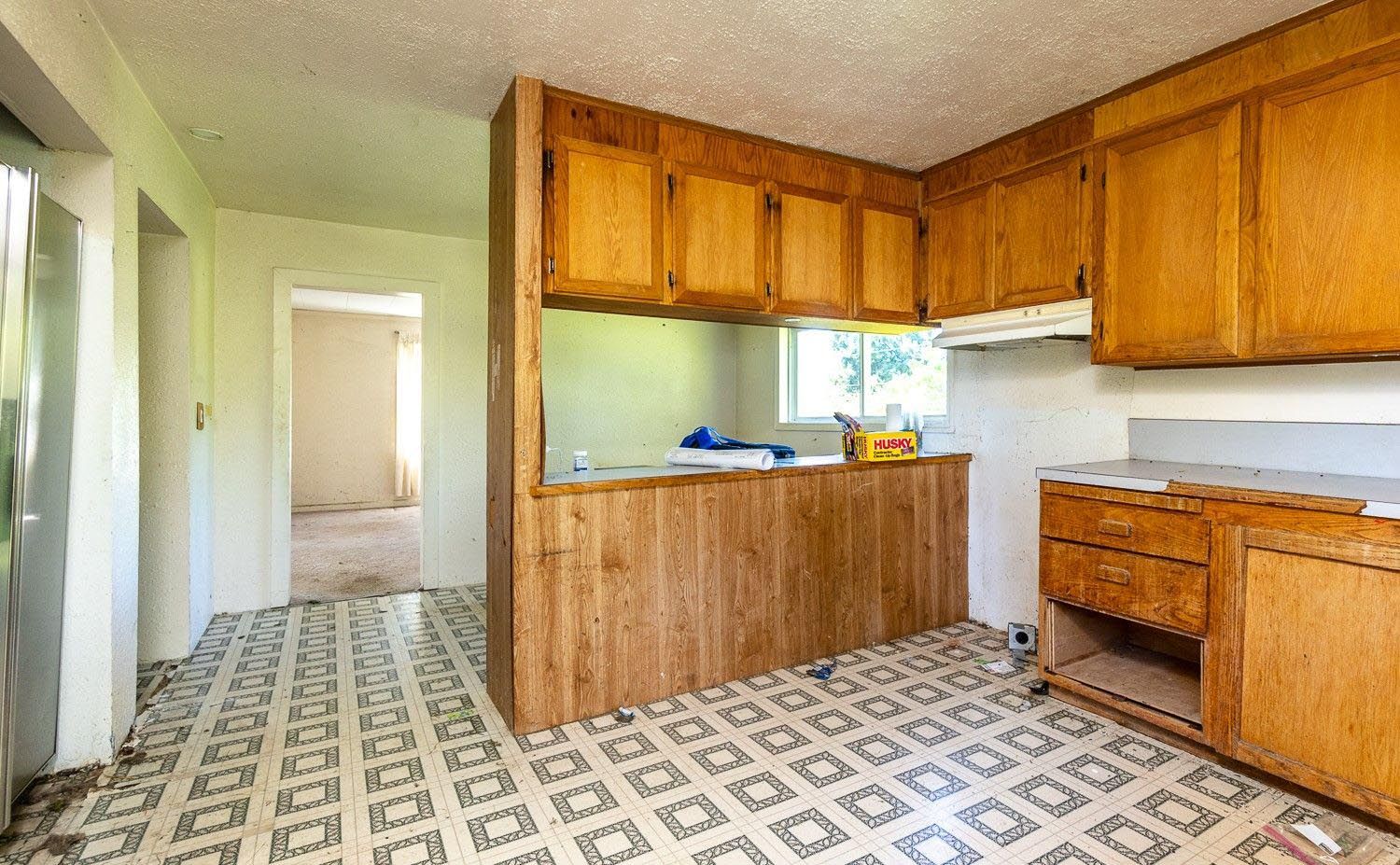 Kitchen with wooden cabinets, light-colored countertops, and patterned tile flooring; doorway to another room.