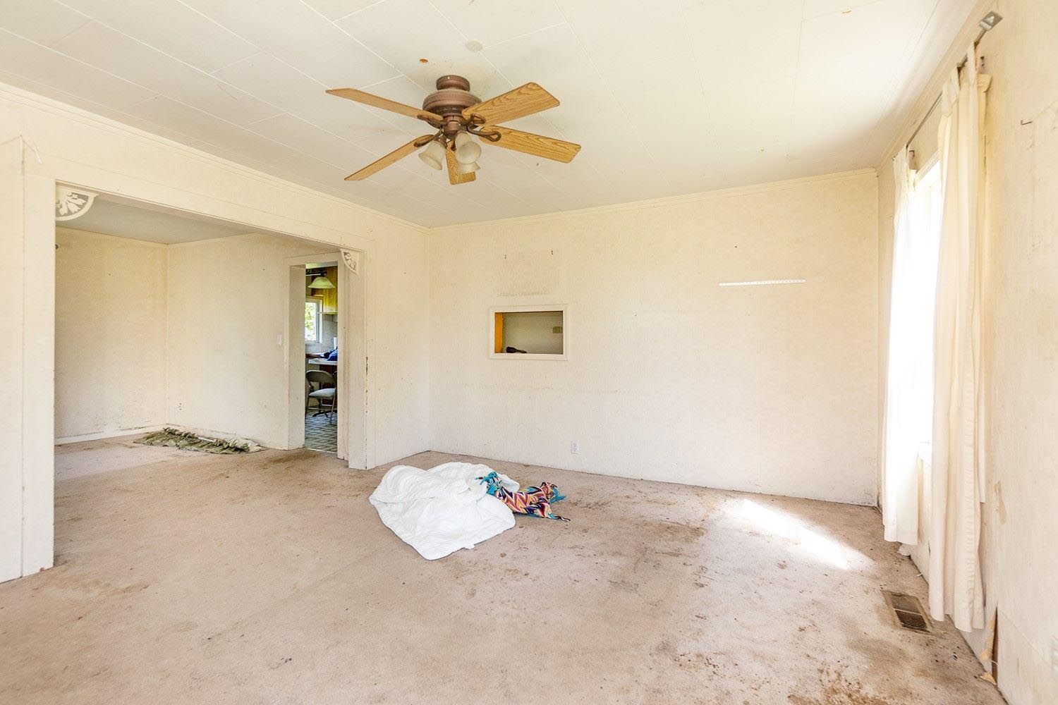 Empty, dirty room with stained carpet, a ceiling fan, and a view into another room.