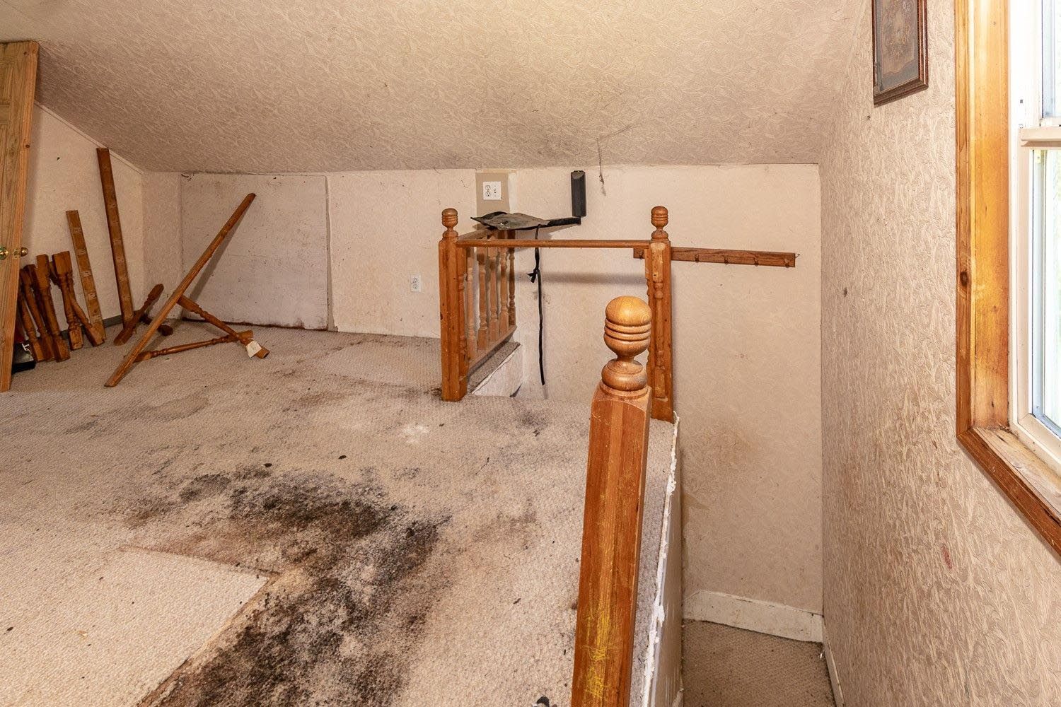 Interior view of a dusty attic with a wooden staircase and unfinished walls.