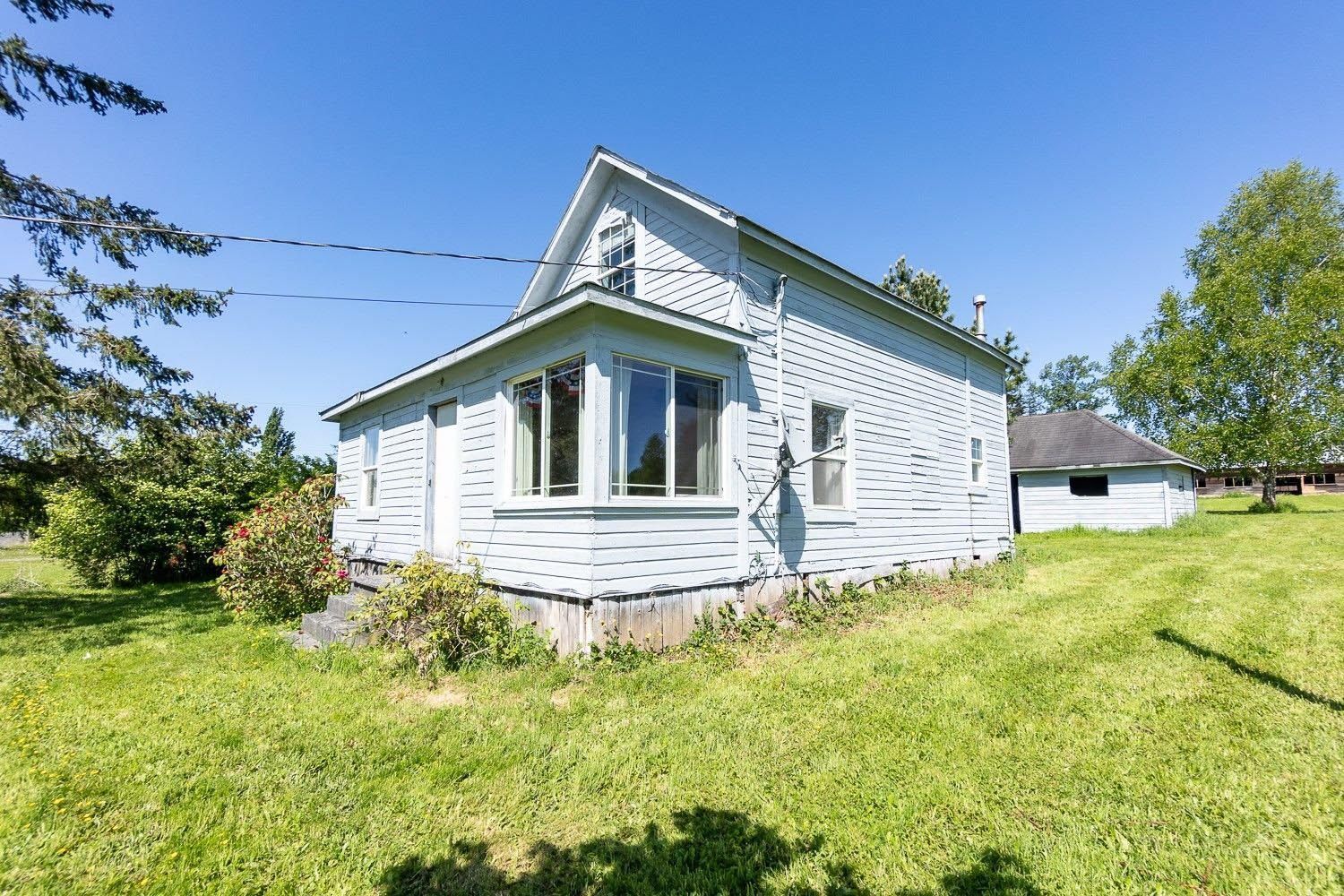 Light blue house with a bay window, set on a grassy lot, under a bright blue sky.