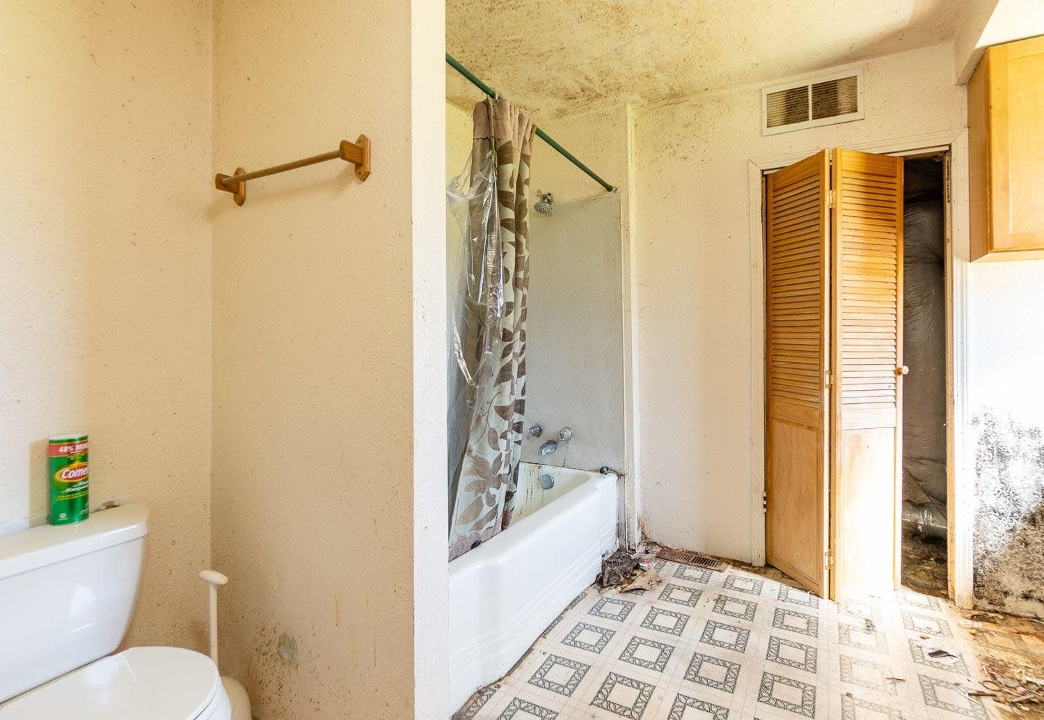 Dirty bathroom with mold on walls and ceiling; toilet, tub, and folding door are visible.