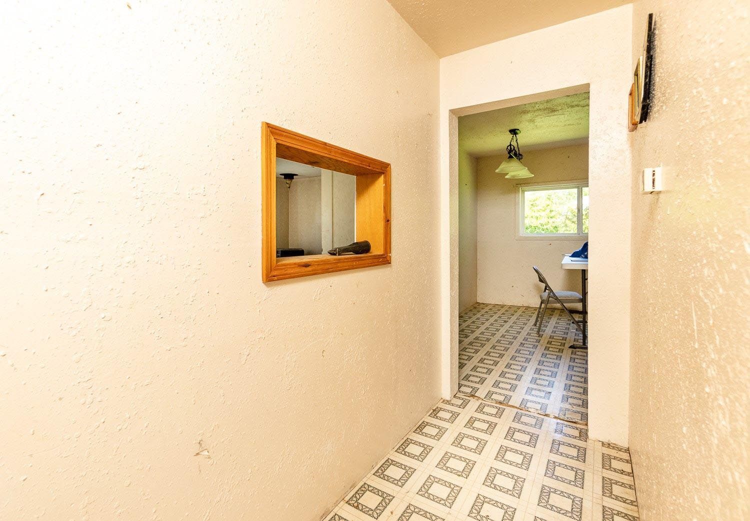 Hallway with a wooden-framed mirror on the left wall and a doorway to a room with patterned flooring.