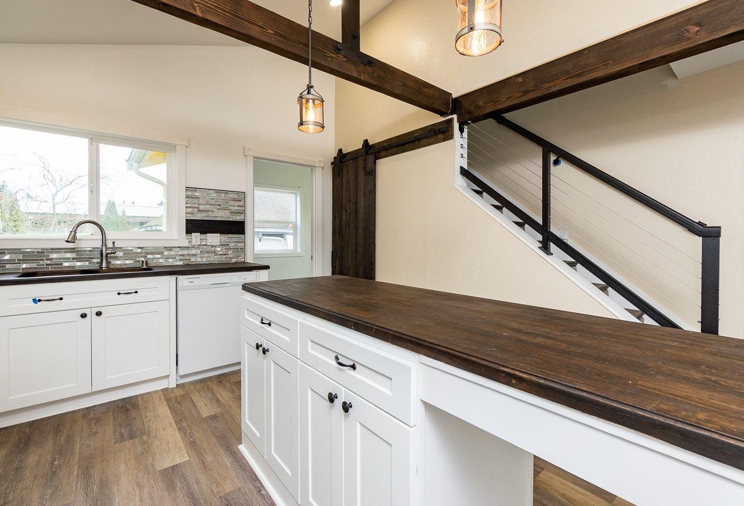 Modern kitchen with white cabinets, dark countertops, wood beams, and a staircase.
