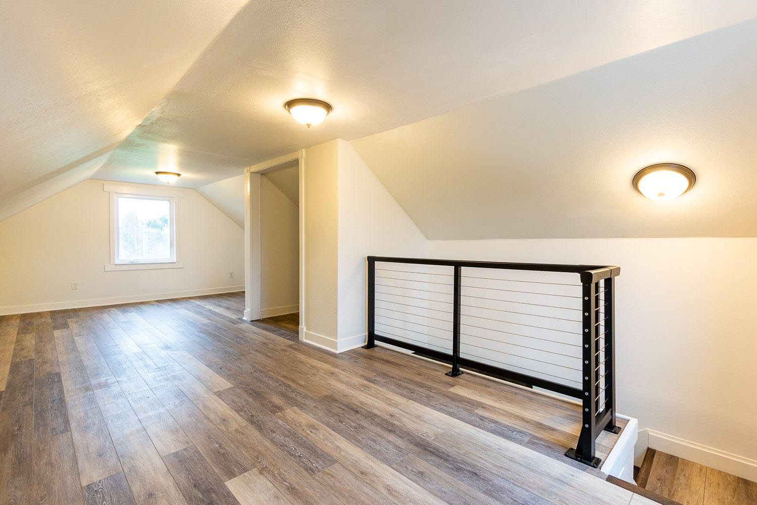 Loft space with hardwood-look floors, white walls, and a black cable railing.