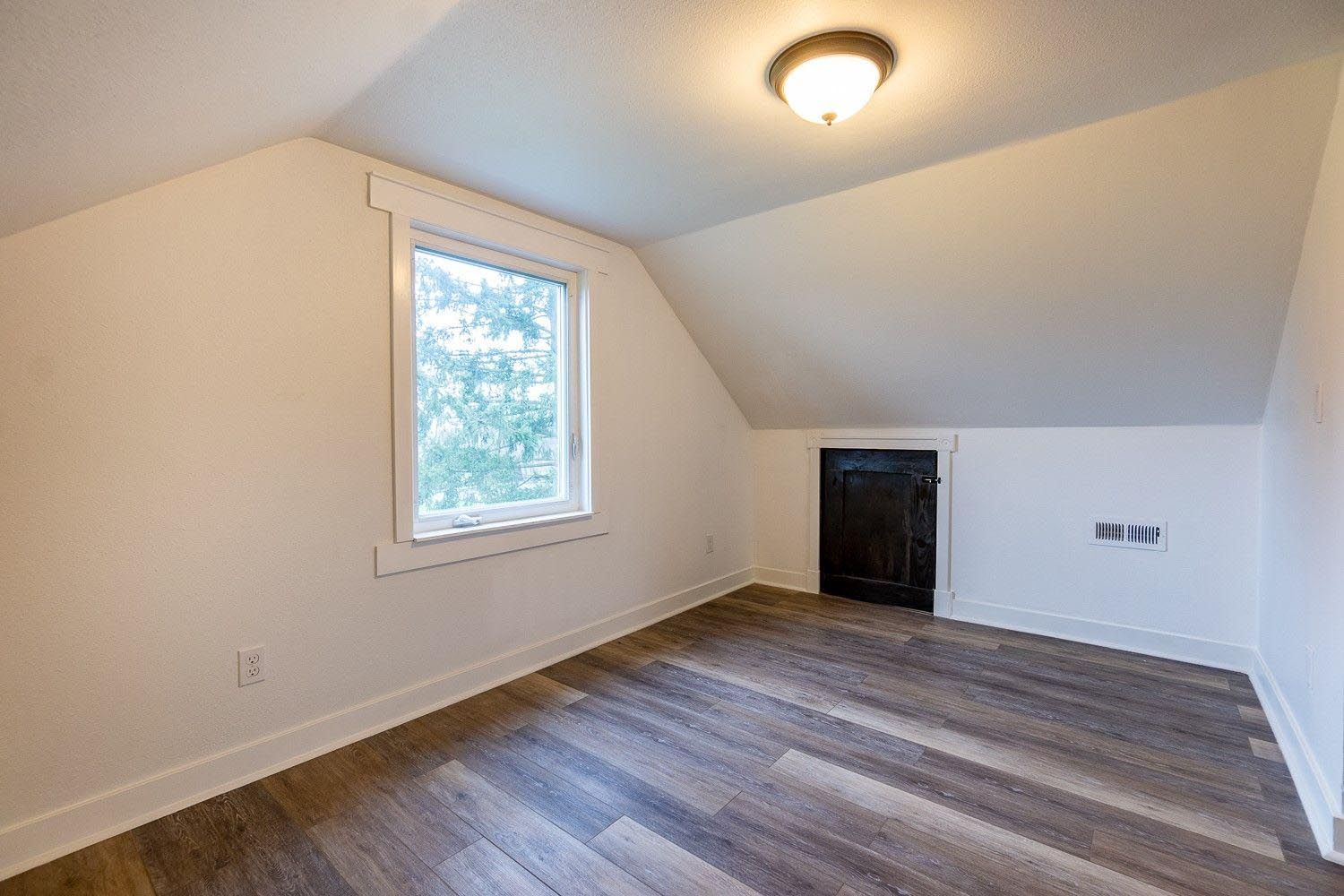 Empty attic room with slanted walls, a window, and wood-look flooring.