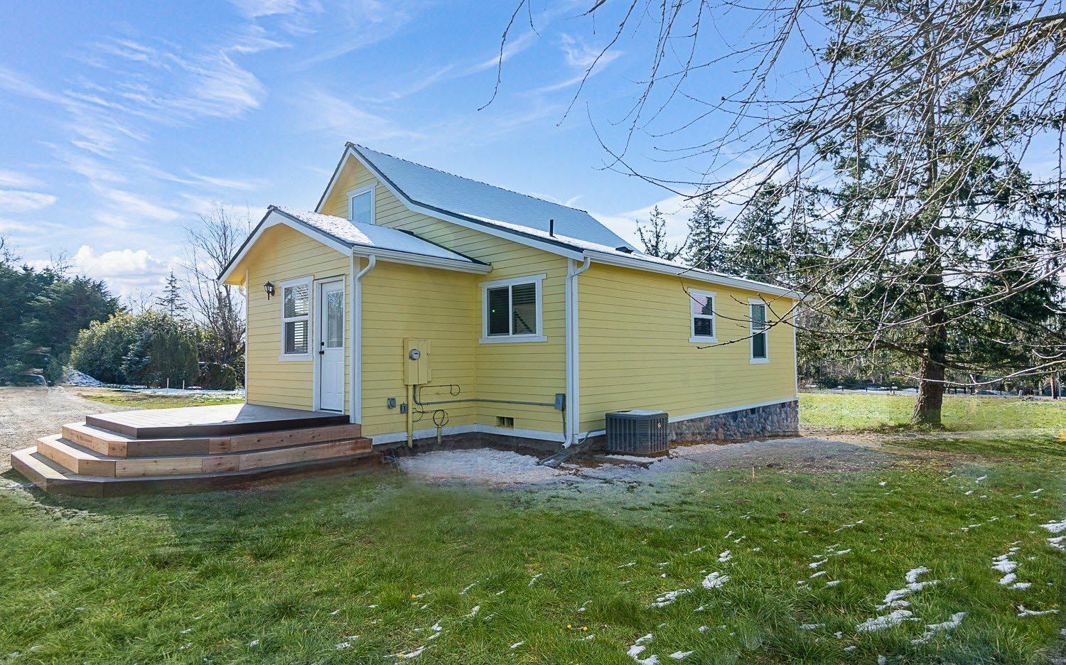 Yellow house with wooden steps, set on green grass with a blue sky background.