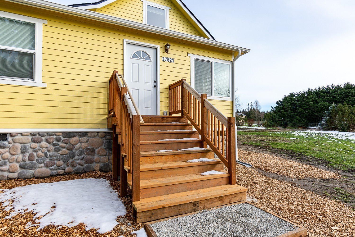 Yellow house with wooden stairs leading to the front door, snow on the ground.