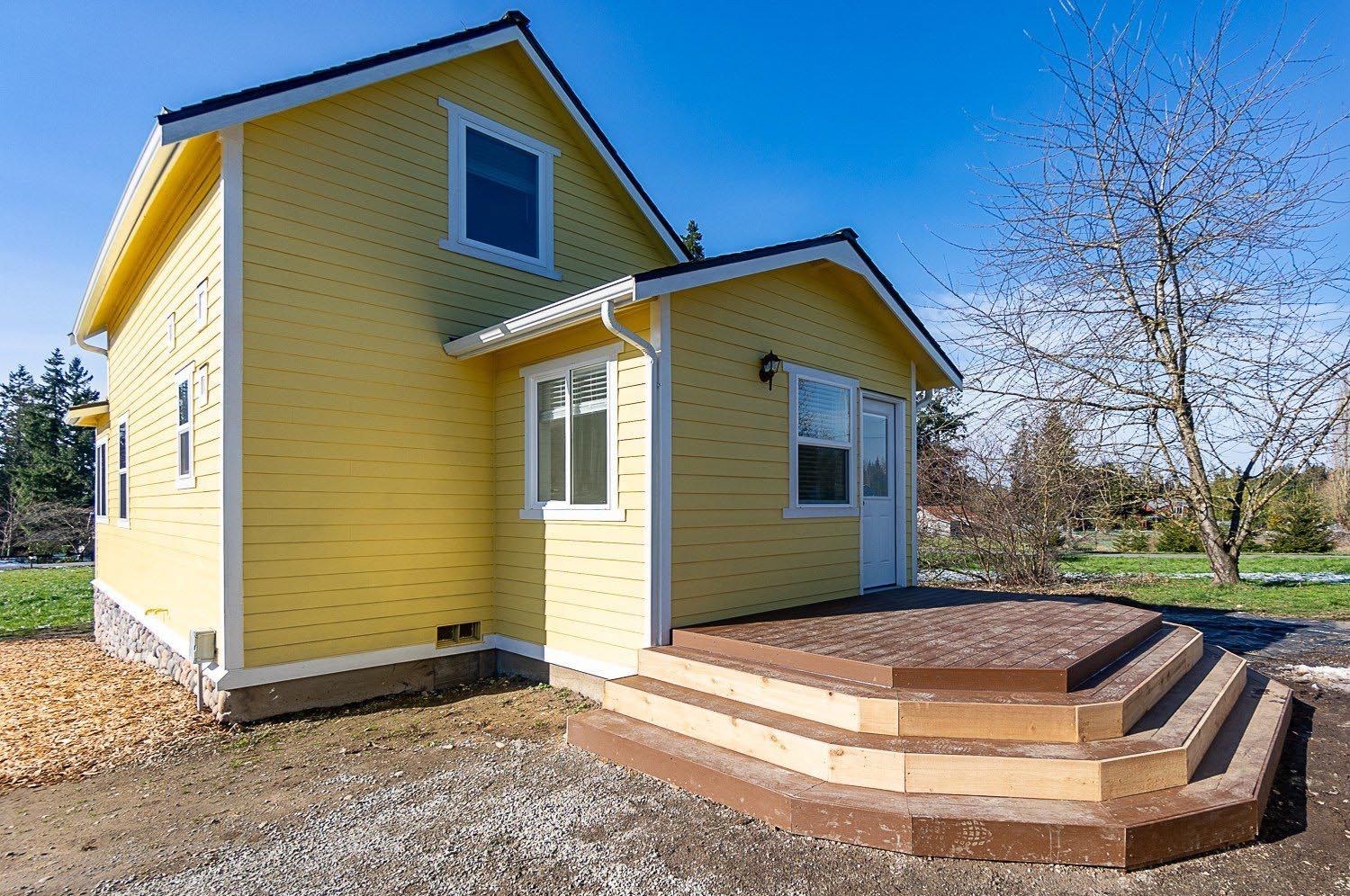 Yellow house with a small deck and steps, under a blue sky.