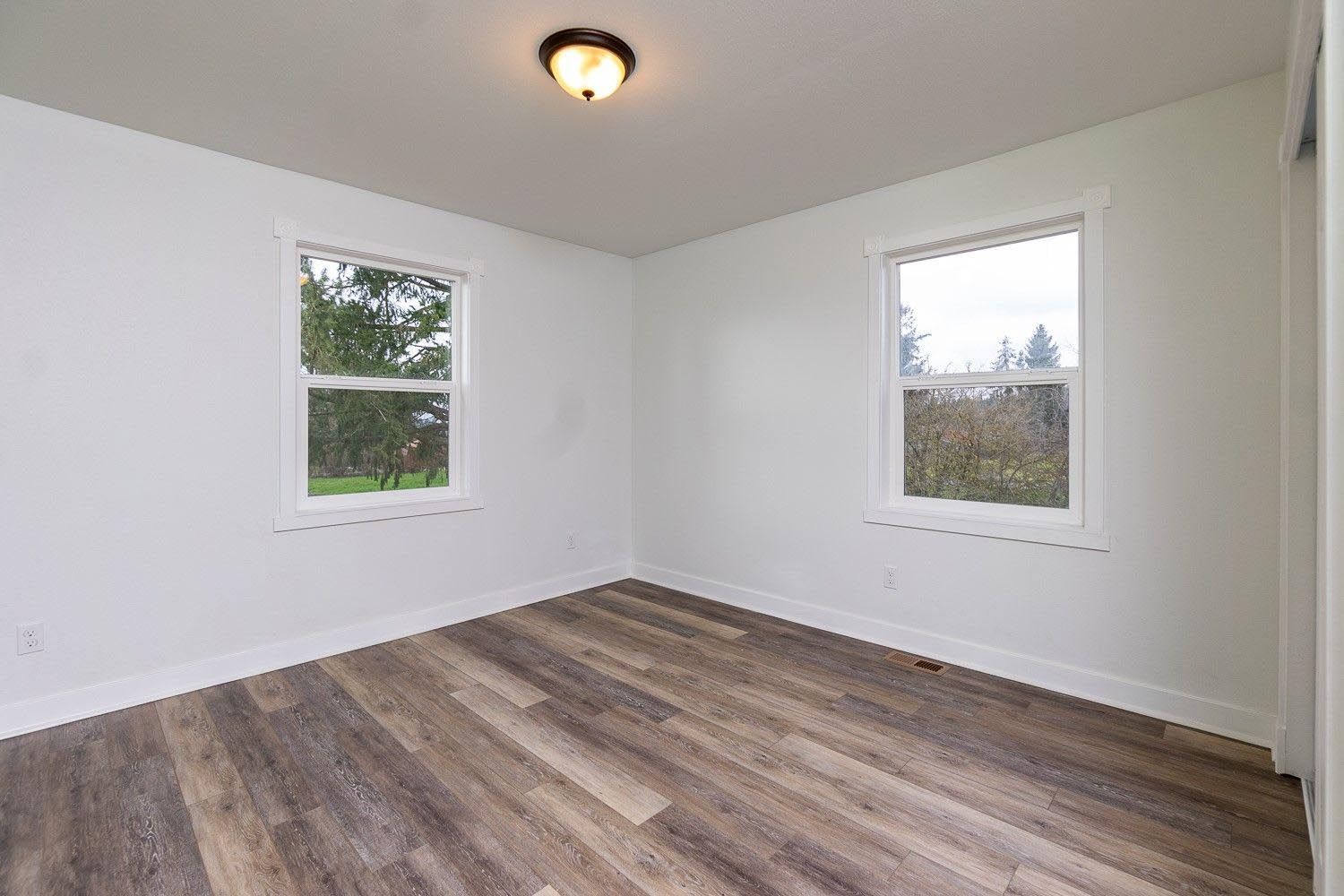 Empty room with white walls, two windows, wood-look floor, and ceiling light.