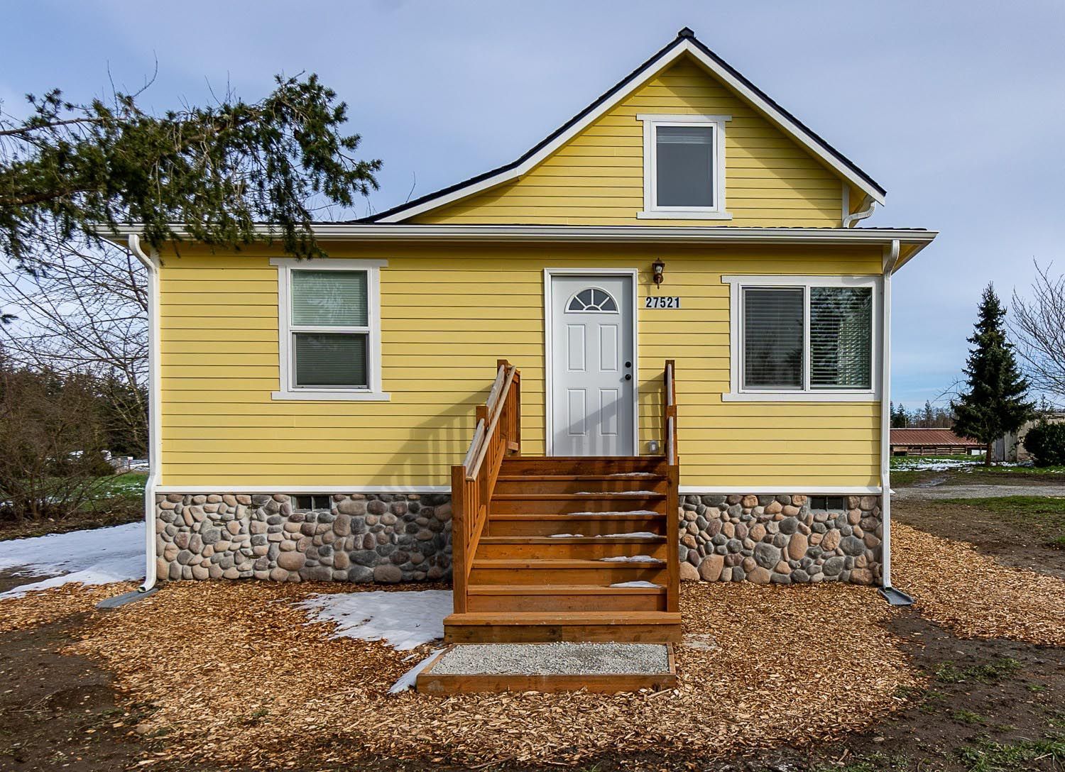 Yellow house with wooden stairs and stone foundation.