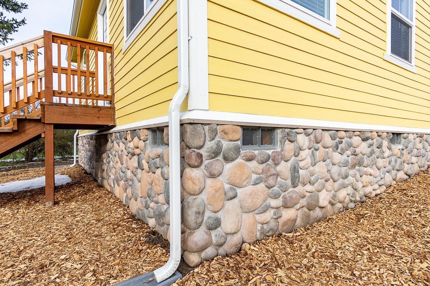 Yellow house with stone foundation, white trim, and a wooden deck.