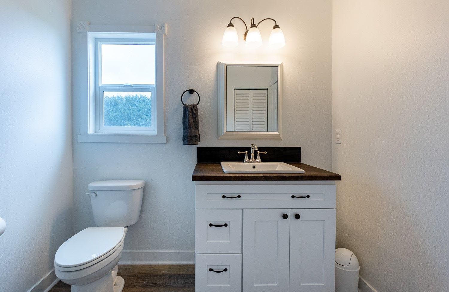 White bathroom with a toilet, vanity, and small window.
