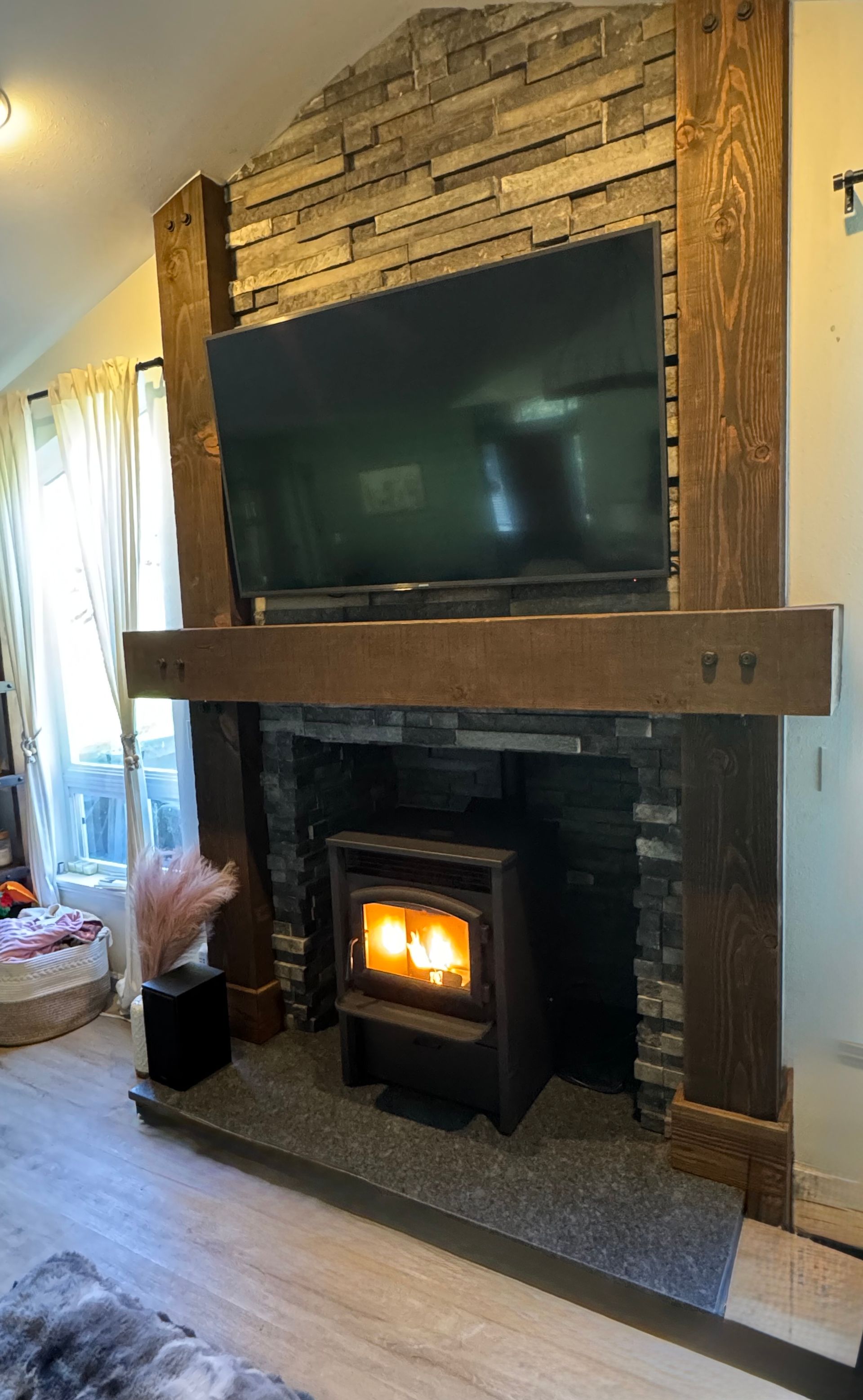 Living room fireplace with large TV above a stone mantel and a lit wood stove insert