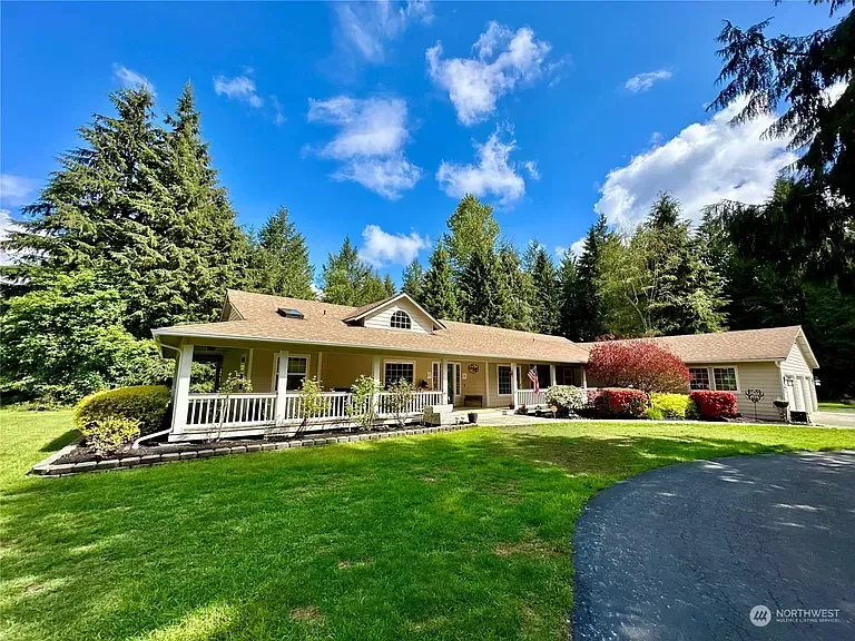 A single-story house with a green lawn, surrounded by trees under a blue sky with clouds.