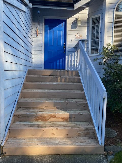 Wooden stairs leading to a blue front door with white railing.