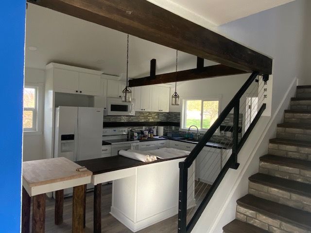 Kitchen with white cabinets, dark wood beams, and a breakfast bar. A staircase is on the right.