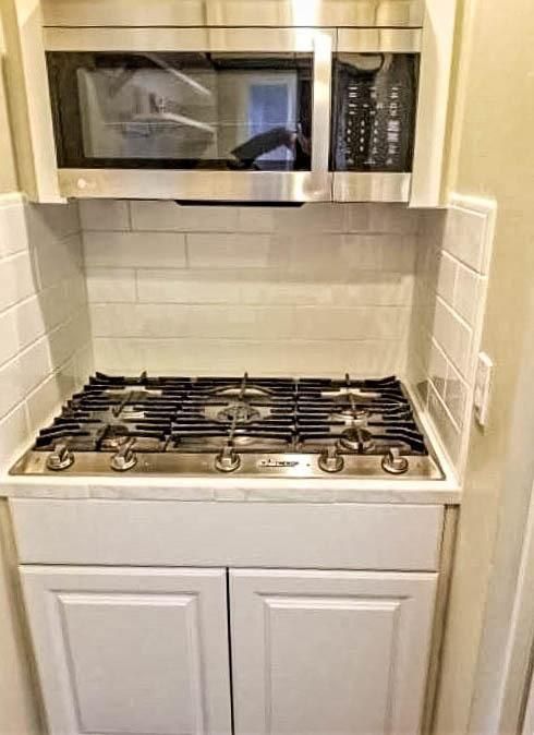 A white kitchen with a microwave over a stovetop with white cabinets.