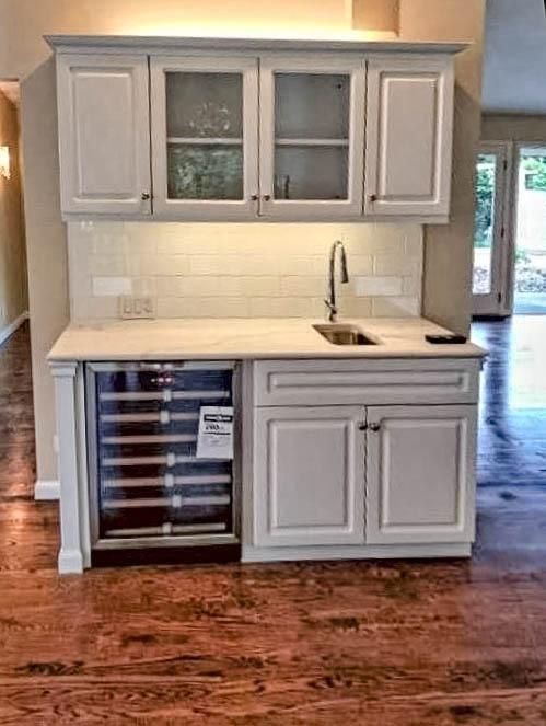 White cabinets with wine fridge and sink, above them glass-fronted cabinets, and a white countertop.